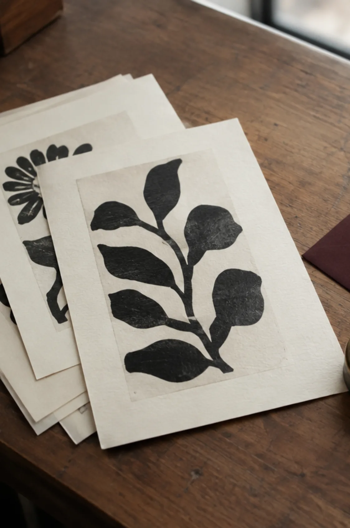 Screen-printed prints in black ink on cream paper, stacked on the counter